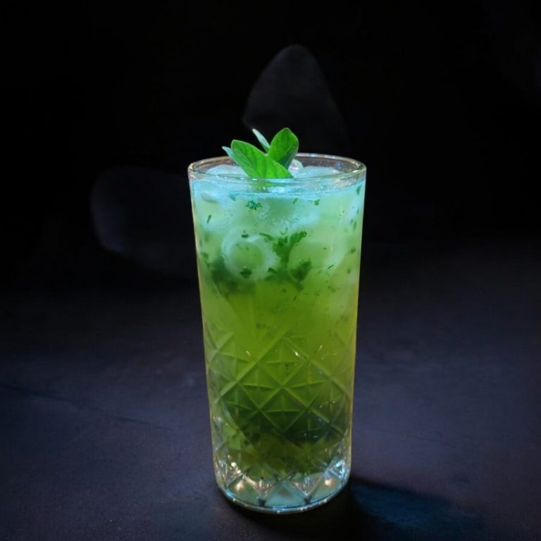Mojito tradicional en vaso de cristal con menta fresca, hielo y color vibrante verde bajo iluminación tenue.