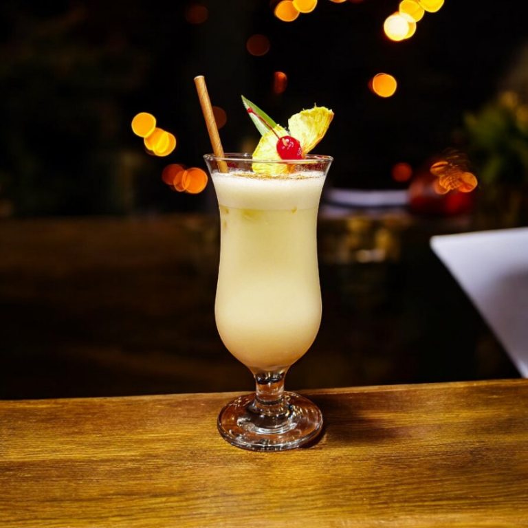 Piña colada servida en copa alta, decorada con piña, cereza y un toque tropical en un ambiente cálido y acogedor.