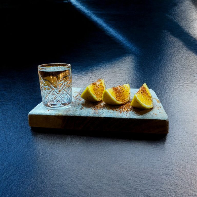 "Botella de mezcal espadín con vaso y rodaja de naranja."